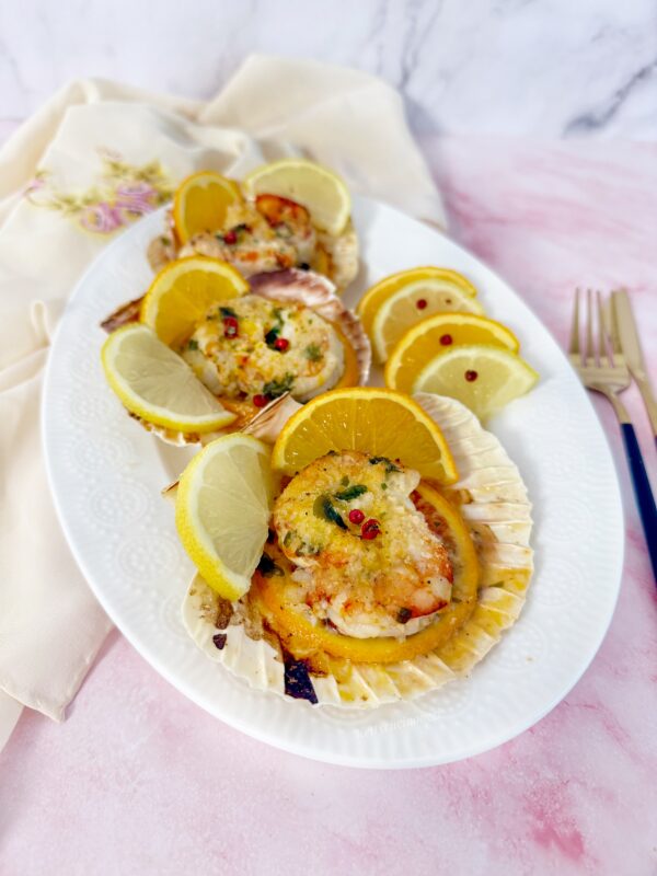 Serviamo i gamberoni all'arancia gratinati ancora caldi, decorandoli con fettine di arancia e limone e pepe rosa.